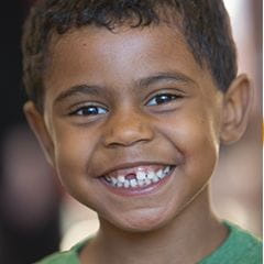 School aged boy with a missing front tooth standing and smiling