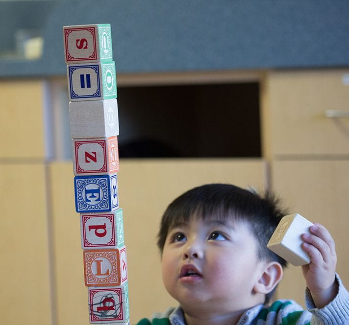 Toddler boy stacking blocks into a tall tower