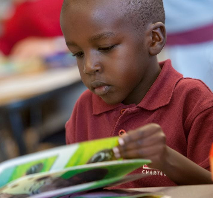 Kindergarten boy reading a book at a desk