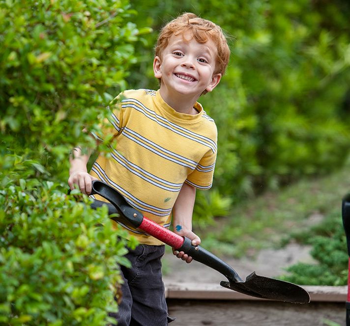 Red-haired Kindergarten Prep boy using a spade in the garden outside
