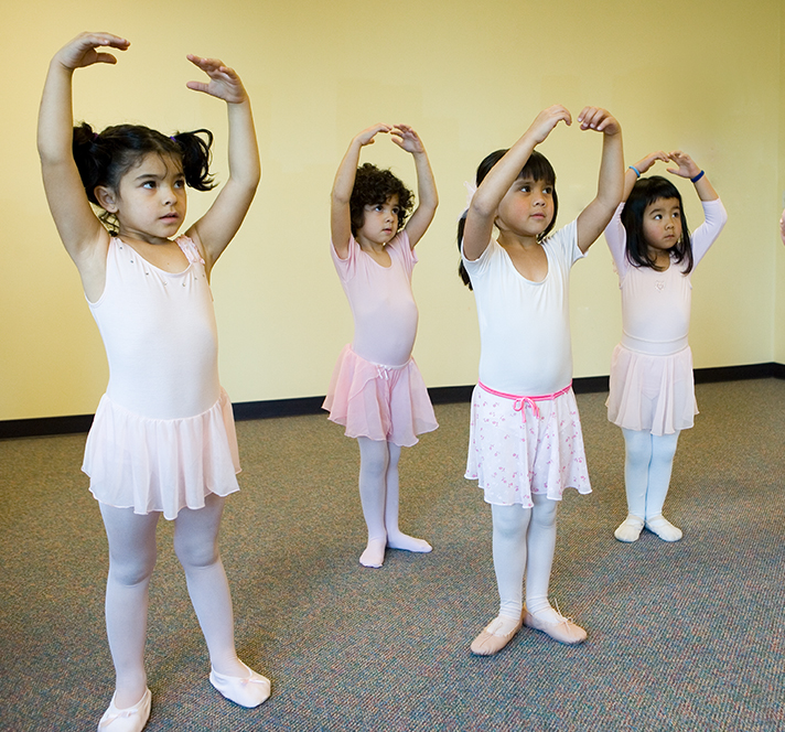 Four Kindergarten aged girls in leotards and tutus practicing ballet
