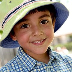 Kindergarten boy wearing a plaid shirt and striped hat outside
