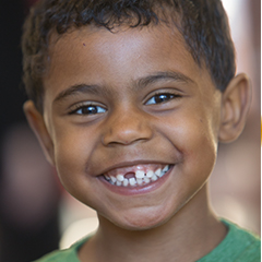 School aged boy with a missing front tooth standing and smiling