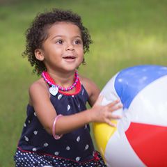 Preschool girl holding a big beach ball outside