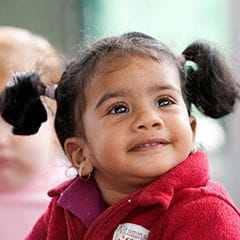 Toddler girl in a pink coat and two pigtails looking up and smiling