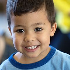Brown-haired boy in his twos wearing a blue shirt and smiling