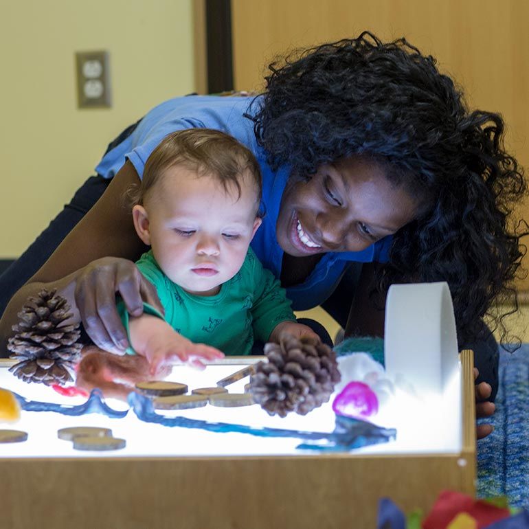 Bright Horizons infant and teacher examining items from nature
