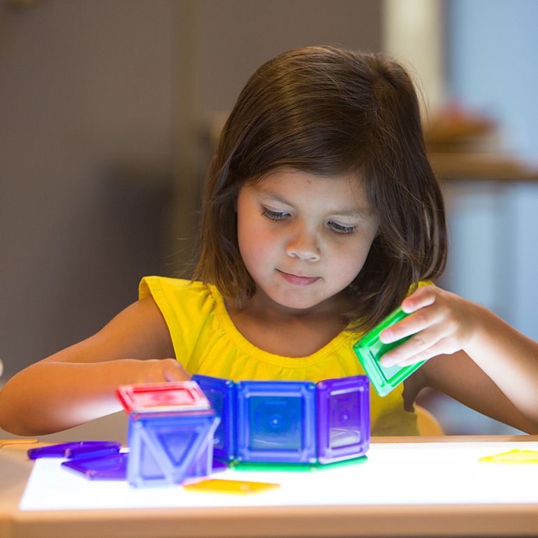 A preschool girl playing with math squares on a light table
