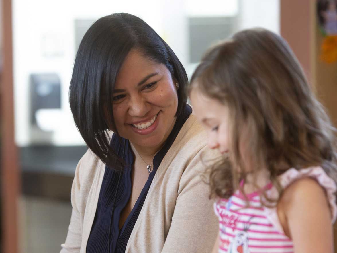 Teacher smiling with a preschool aged girl in a center