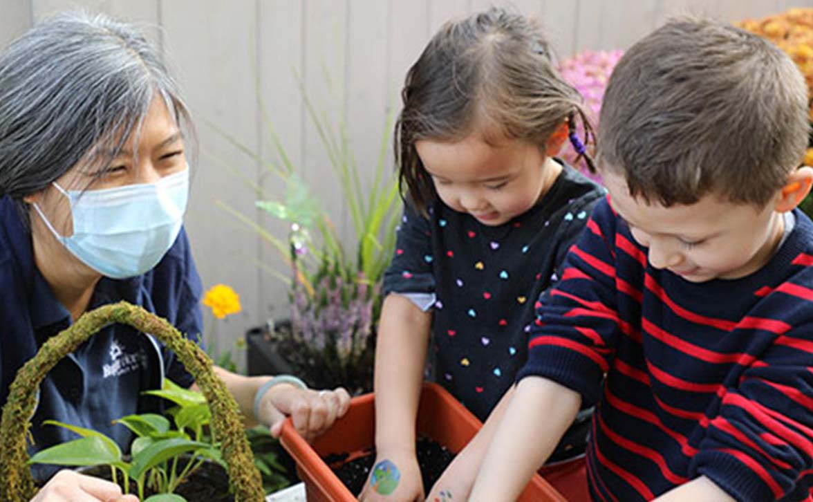 teacher with mask on looking over children playing in garden at daycare | Bright Horizons childcare 