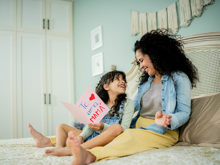 A mother and daughter smiling at each other while reading a book
