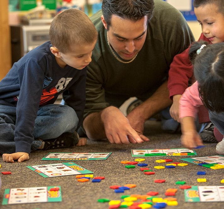 Male teacher sitting on the floor with Kindergarten prep students teaching a math activity