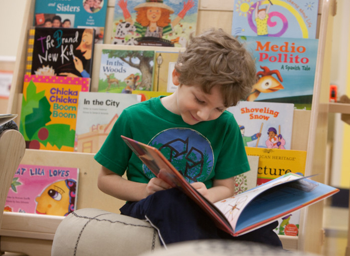 Kindergarten boy sitting and reading in a child care center